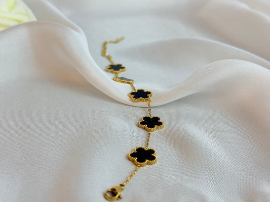 Gold necklace with black clover-shaped pendants on a white fabric background