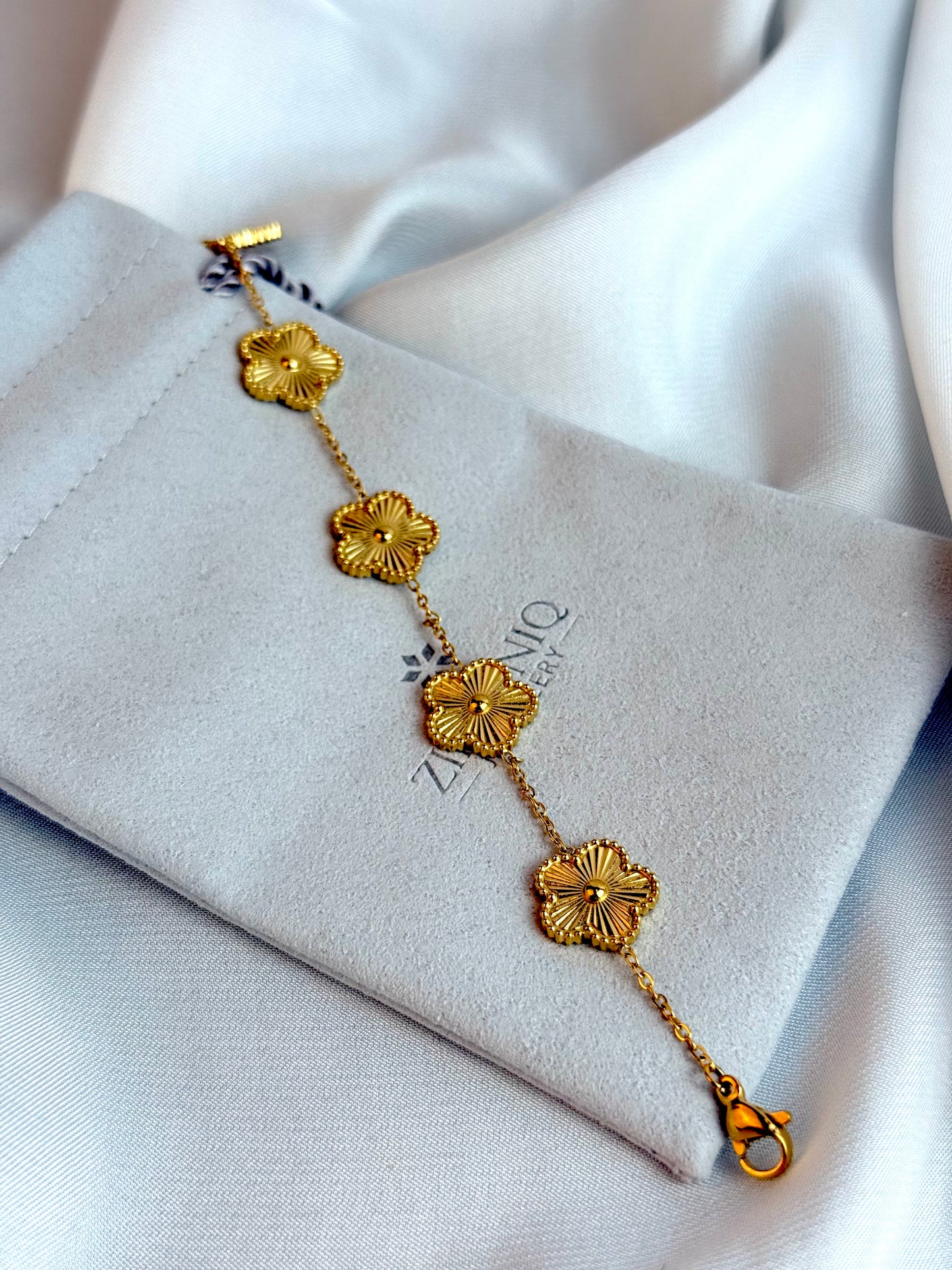 Gold bracelet with floral designs on a Zirconiq branded pouch.