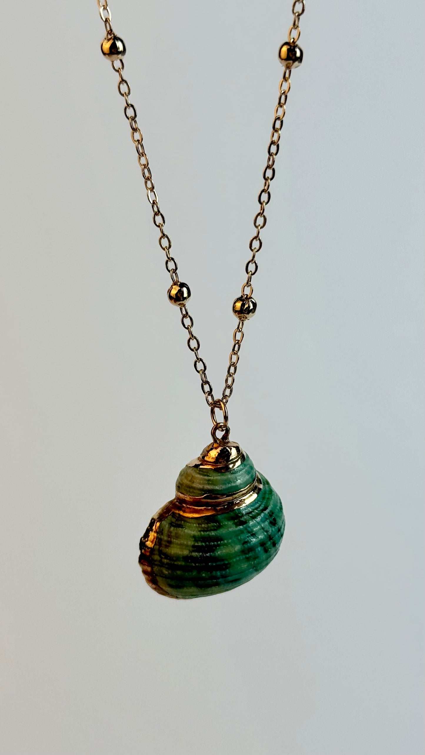 Necklace with a green shell pendant on a light gray background