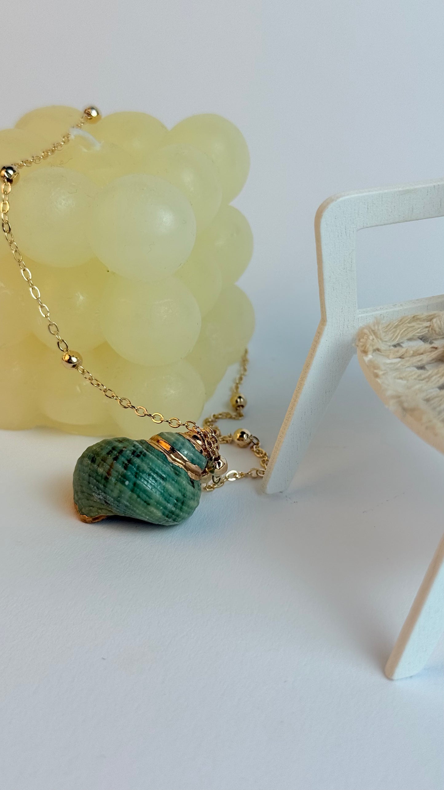 Green shell pendant on a gold chain with a white background