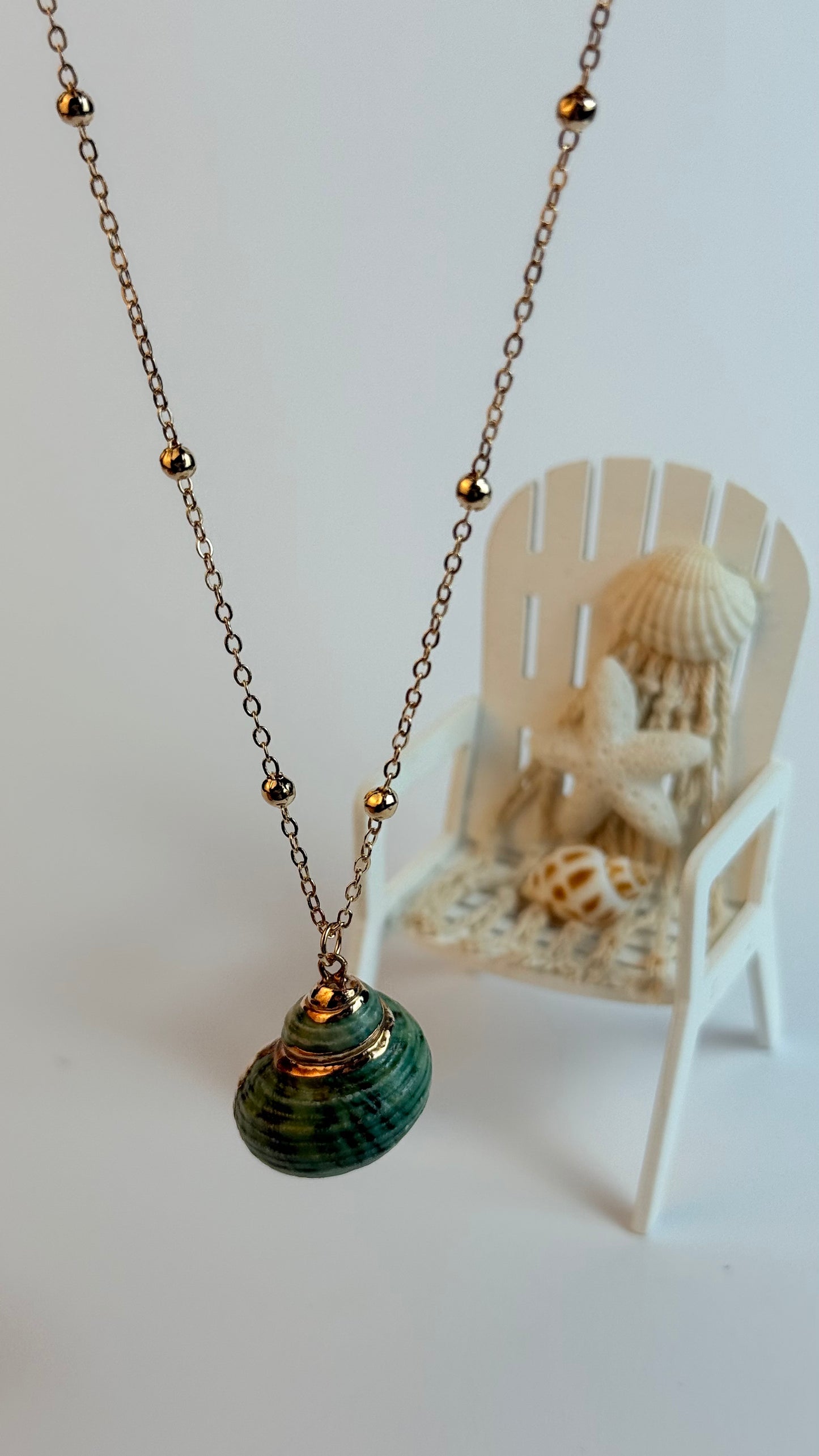 Necklace with a green pendant on a white surface with a small chair and shells in the background