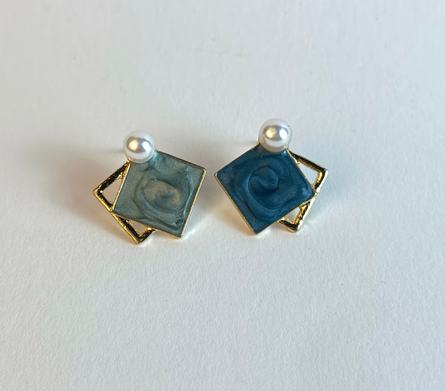 Pair of square earrings with blue centers and gold borders on a white background