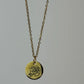 Gold necklace with a round pendant featuring a rose design on a gray background