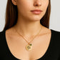 Woman wearing a gold necklace with a pendant on a plain background