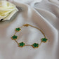 Gold bracelet with green clover-shaped charms on a white fabric background