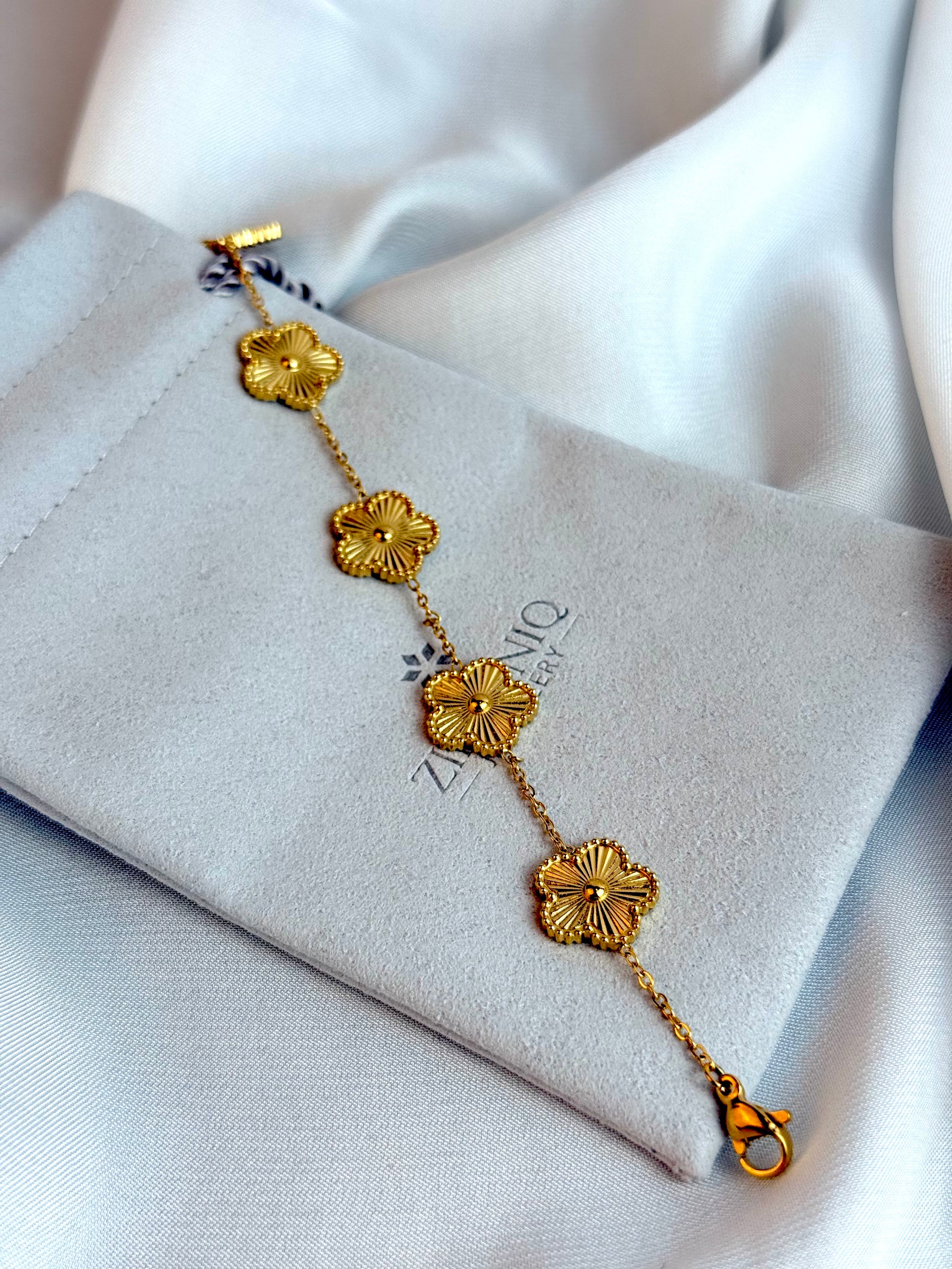 Gold bracelet with floral designs on a Zirconiq branded pouch.