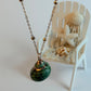 Necklace with a green pendant on a white surface, with a small chair and shells in the background.