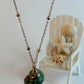 Necklace with a green pendant on a white surface with a small chair and shells in the background
