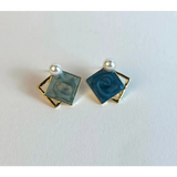 Pair of square earrings with blue centers and gold borders on a white background