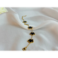 Gold necklace with black clover-shaped pendants on a white fabric background