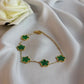 Gold bracelet with green clover-shaped charms on a white fabric background