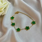 Gold bracelet with green clover-shaped charms on a white fabric background