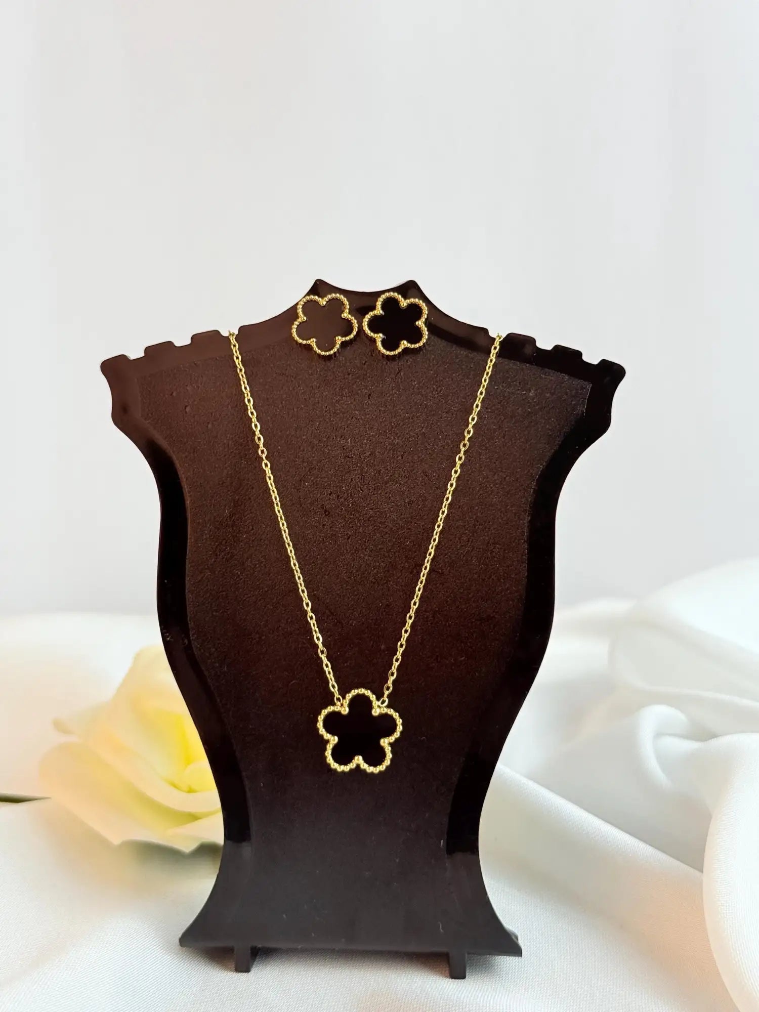 Gold four-leaf clover necklace with matching earrings displayed on a dark brown mannequin stand.